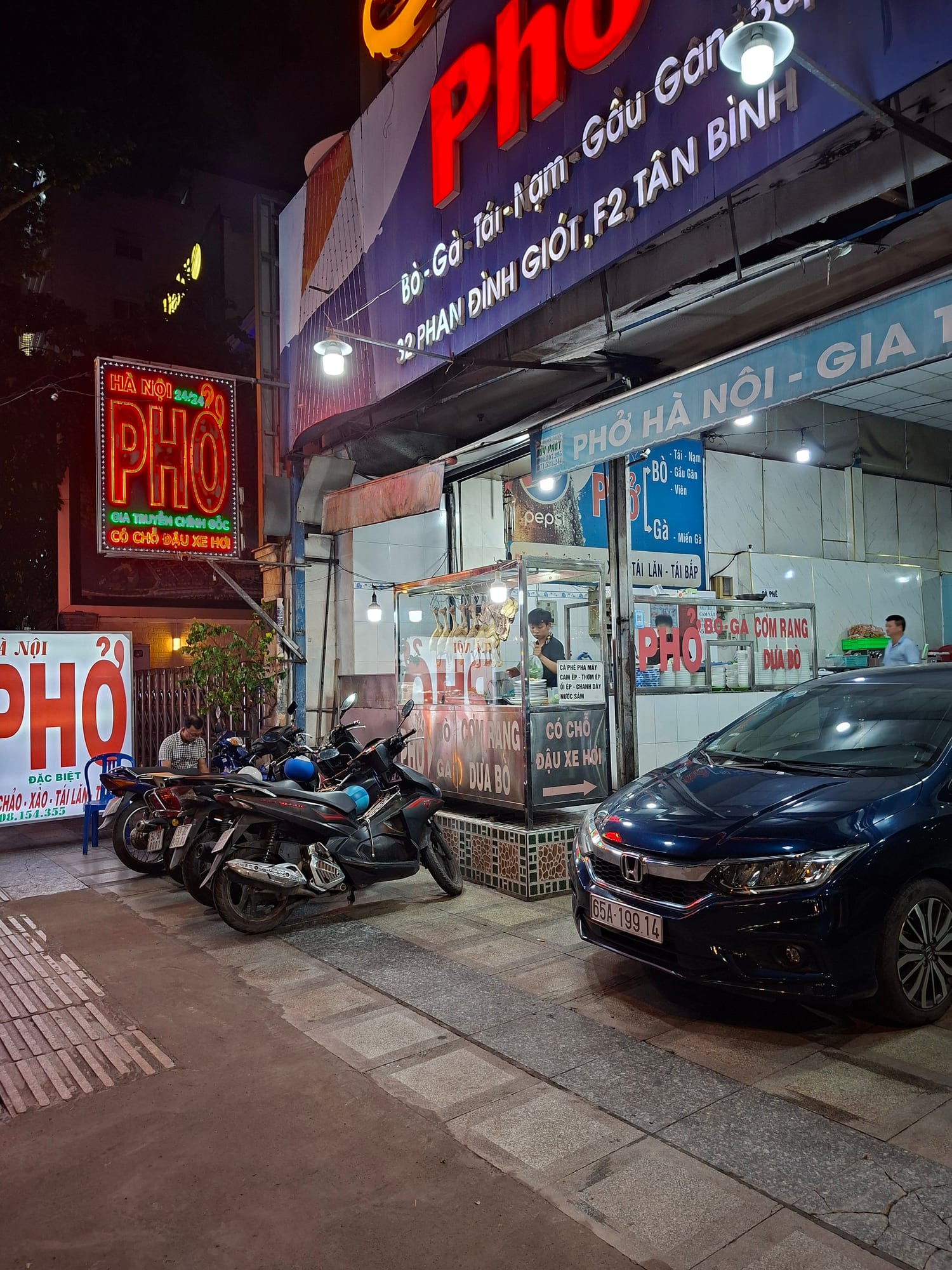 The restaurant at night, illuminated signage glowing against the dark street with motorcycles parked outside