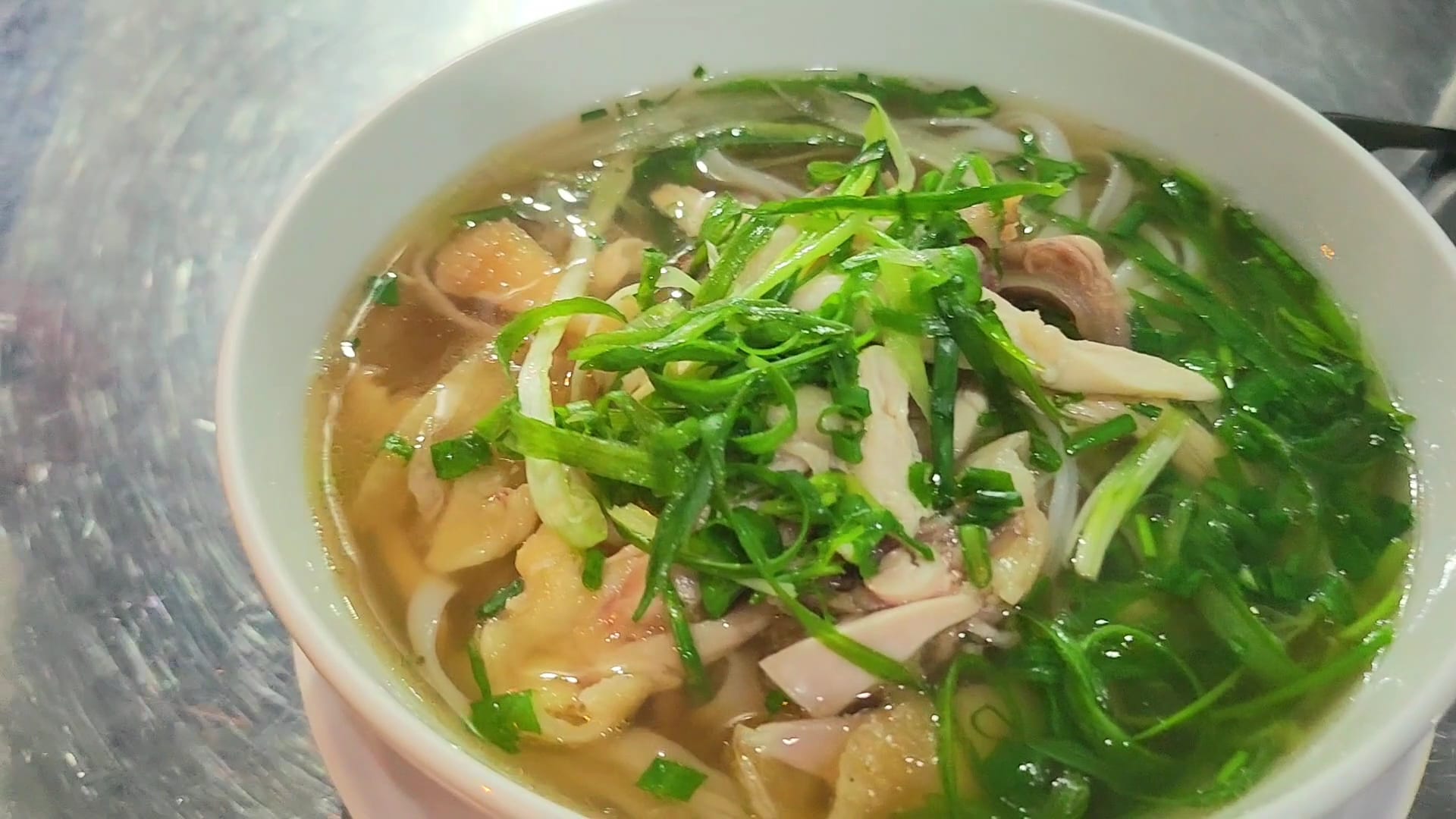 A steaming bowl of Vietnamese phở with rice noodles, meat, and fresh green onions