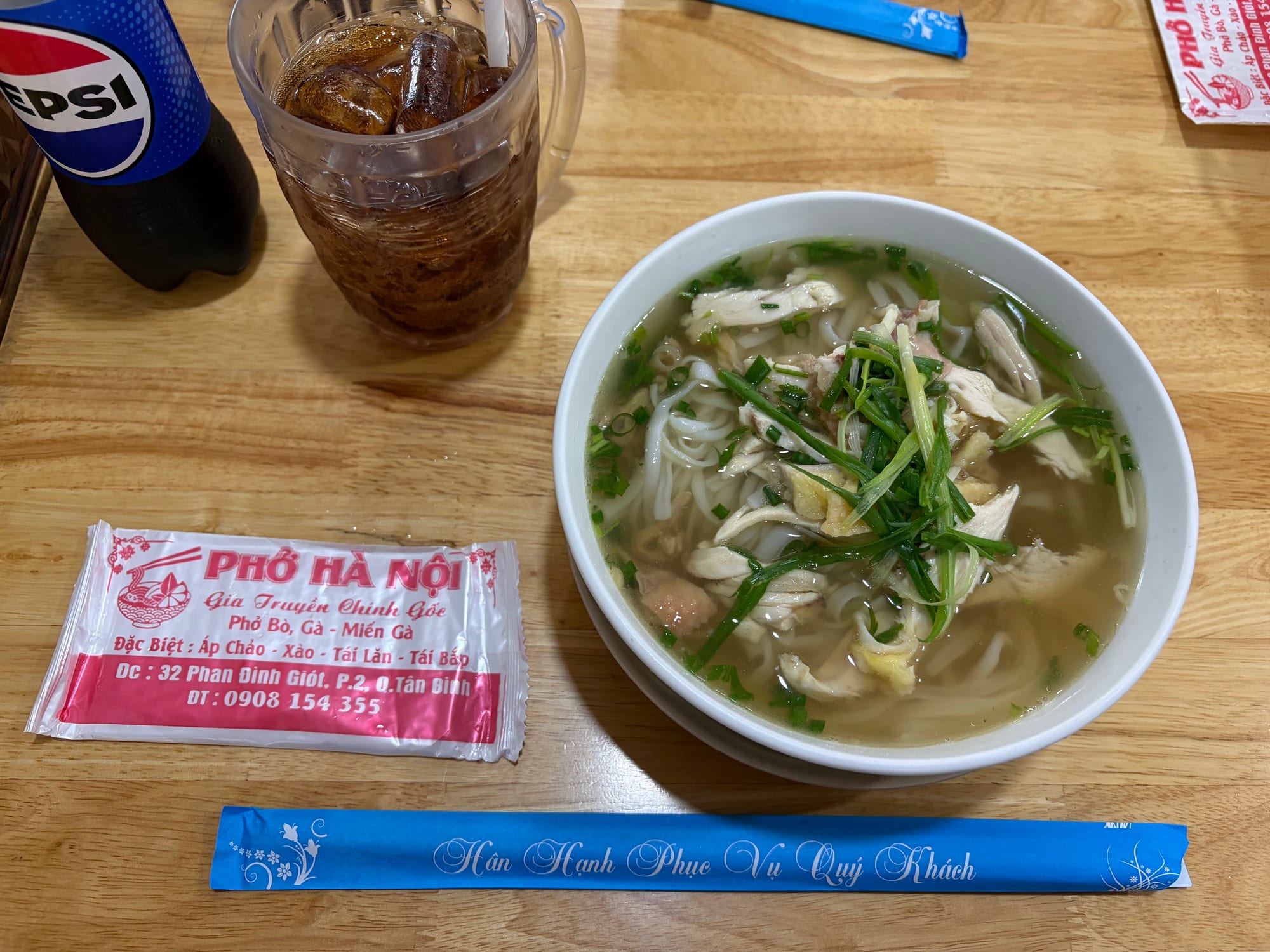 A bowl of Vietnamese phở with chicken and rice noodles served on a wooden table